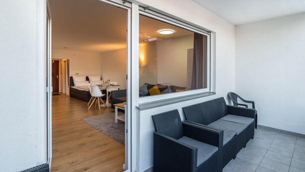 Une porte coulissante donne sur un espace de vie comprenant un canapé, des fauteuils et une table à manger.