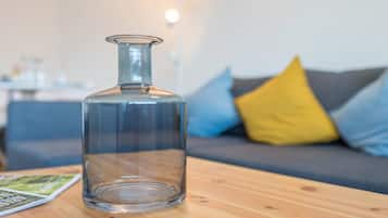 Una botella de vidrio transparente sobre una mesa de madera, con una revista, y un sofá con cojines al fondo.