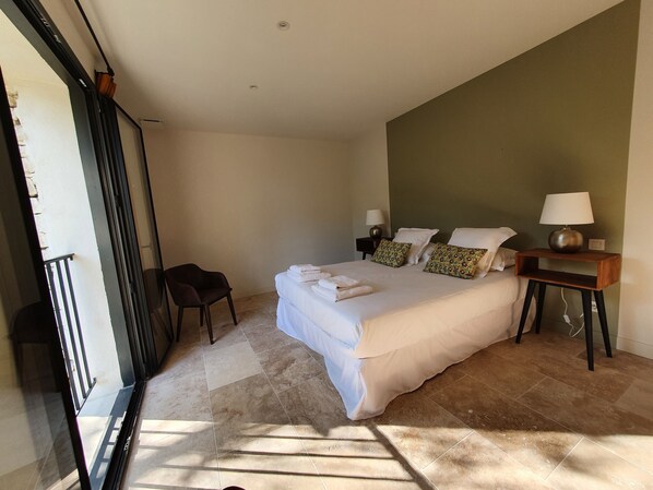 A bedroom with a bed, a chair, a nightstand, and a lamp.