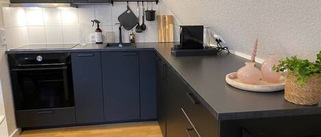 Una cocina moderna con armarios oscuros, un horno empotrado y una encimera con microondas.