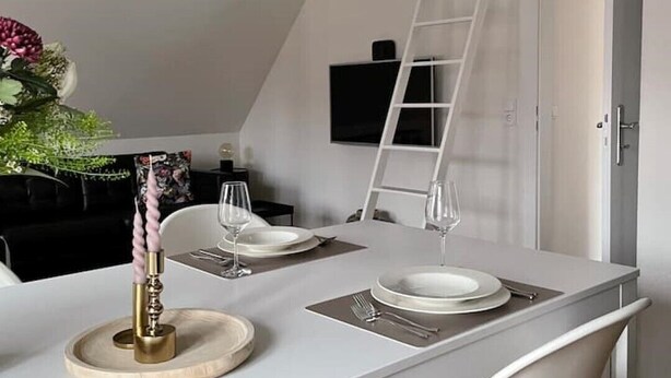 Et moderne spiseområde med et hvidt bord, hvide stole, en sort hængende lampe og en hvid stige.