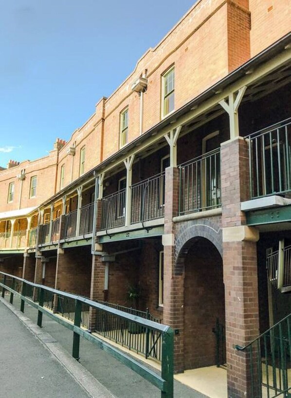A multi-story building with a brick facade, balconies with metal railings, and a covered walkway.