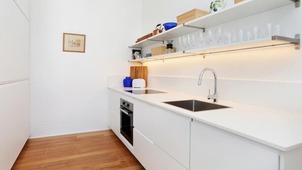 A compact kitchen with white cabinetry, a built-in oven, a sink, and a wooden countertop.