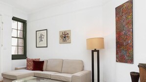 A living room with a beige sofa, two framed artworks, a floor lamp, and a large abstract painting.
