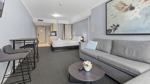 A hotel room with a bed, a sofa, a small table with a vase of flowers, and a painting on the wall.