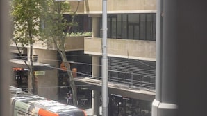 A tram with passengers, a pedestrian walkway, and a building with a sign.