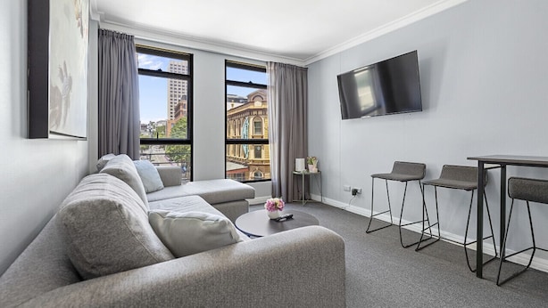 A modern living room with a sofa, a small table, a TV, and a view of a building through large windows.