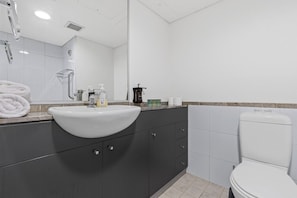 A bathroom with a white sink, dark cabinets, a toilet, and a mirror. - Amazing unit near China Town (Haymarket)
