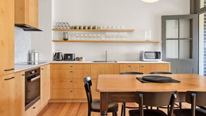 A modern kitchen with wooden cabinets, a built-in oven, a microwave, and a dining area with a wooden table and chairs. - Stylish heritage home The Rocks (The Rocks)