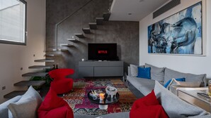 Una sala de estar moderna con una escalera, un televisor de pantalla plana y un cuadro abstracto grande.