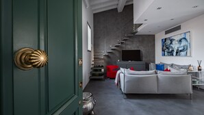 Una sala de estar moderna con un sofá gris, una silla roja y una escalera que sube a un altillo.