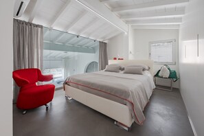 A modern bedroom with a bed, a red chair, a glass partition, and a view of the outdoors.
