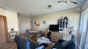 Una sala de estar con dos sofás azules, un televisor, una pequeña mesa de comedor y una estantería.