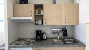 Cocina compacta con estufa, horno y pileta. Hay gabinetes de madera y un pequeño estante con objetos decorativos.