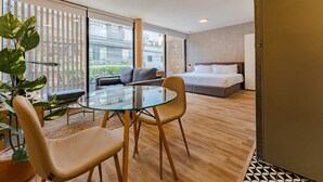 A modern hotel room with a glass dining table, two chairs, a sofa, a bed, and a large window with a view of buildings. - Condesa Cholula Lofts by VH (Mexico City)
