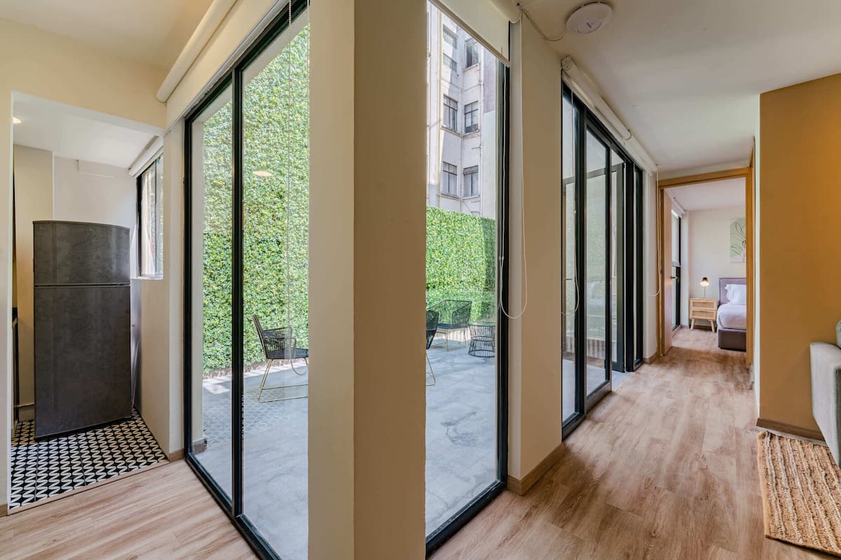 A modern apartment with large sliding glass doors leading to a balcony, a wooden floor, and a visible outdoor seating area.