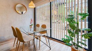 A modern dining area with a glass table, two chairs, a round mirror, and a large potted plant. - Condesa Cholula Lofts by VH (Mexico City)