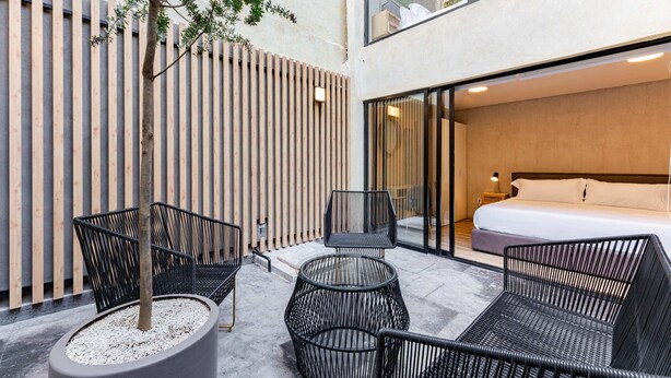A modern hotel room with a large bed, a seating area with chairs, and a view of the city. - Condesa Cholula Lofts by VH (Mexico City)