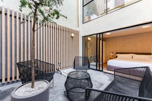 A modern hotel room with a large bed, a seating area with chairs, and a view of the city. - Condesa Cholula Lofts by VH (Mexico City)