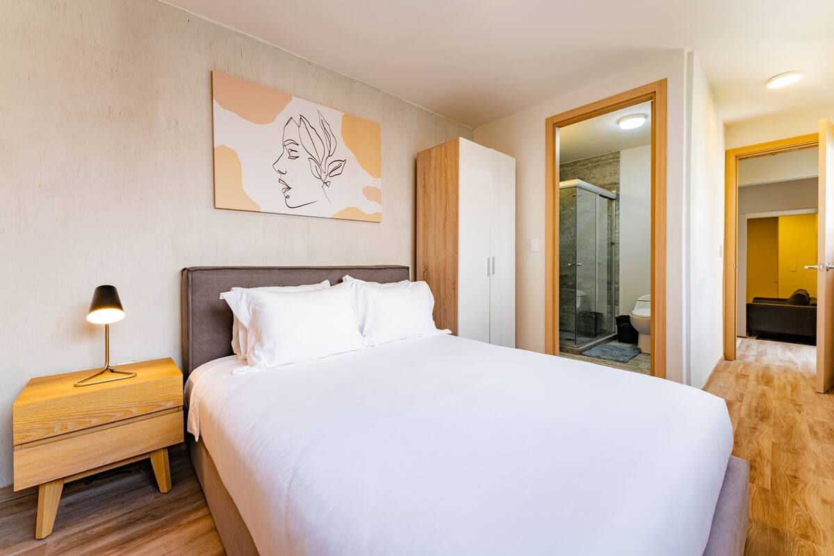 A neatly arranged bedroom with a bed, bedside table, and a wall-mounted artwork.