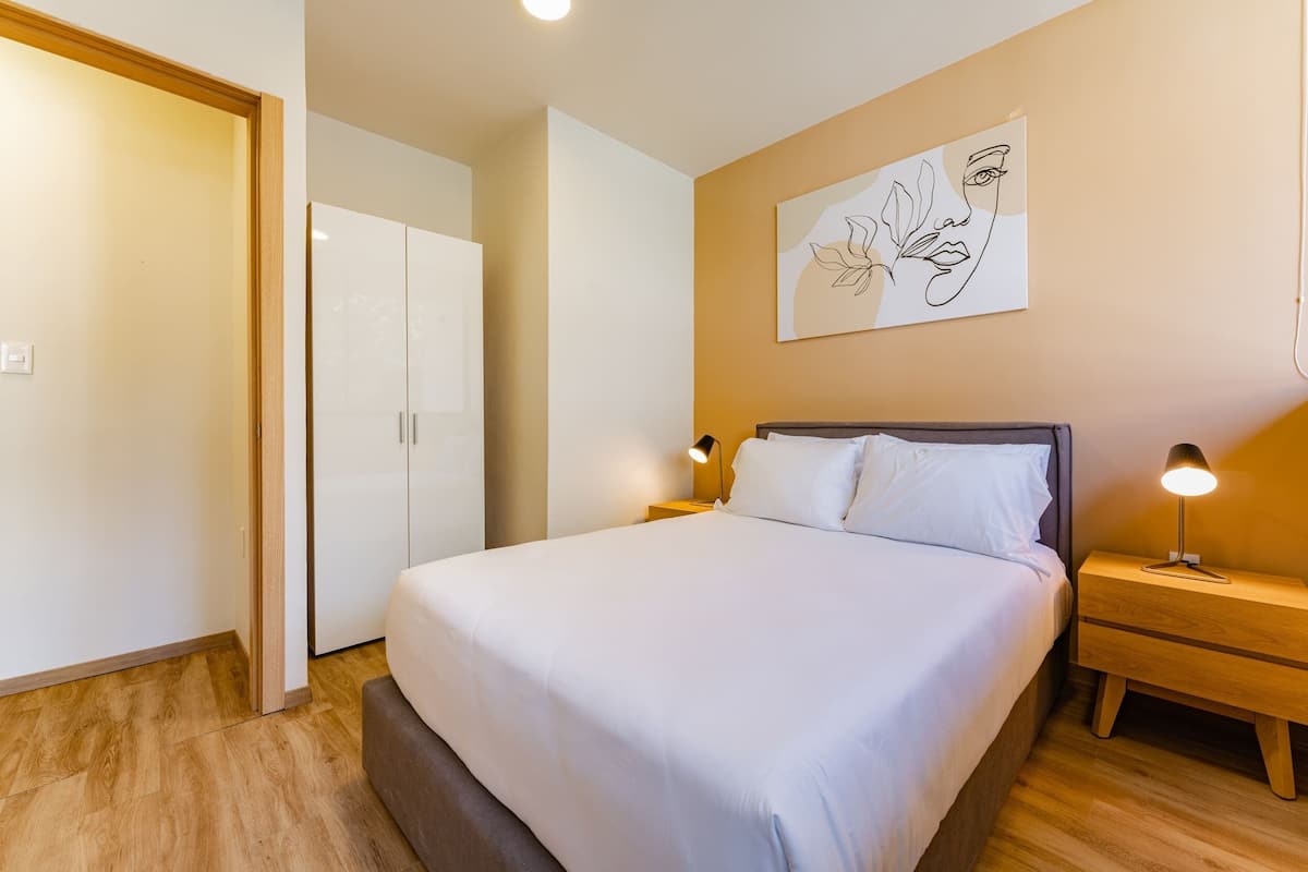 A neatly made bed with white linens, a bedside lamp, and a wall art piece.