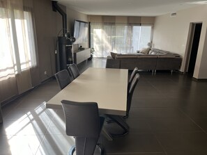 Ein modernes Wohnzimmer mit großem Esstisch, bequemen Sitzgelegenheiten, einem Kamin und großen Fenstern für natürliches Licht.