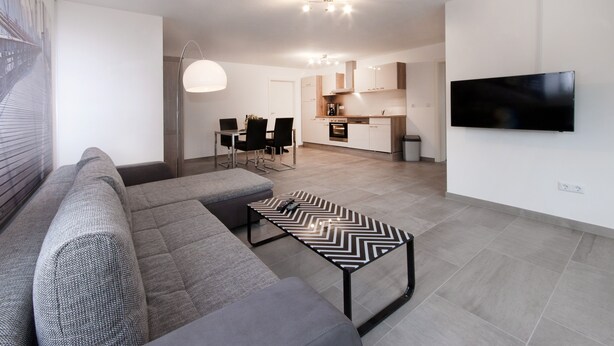 A modern living room with a grey sofa, a black and white chevron-patterned coffee table, and a flat-screen TV mounted on the wall. - Moderne Ferienwohnung in Öhringen mit Idealer Anbindung zur Autobahn (Öhringen)