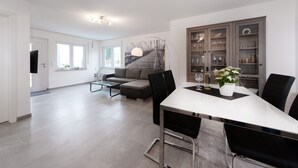 A modern living room with a sofa, a dining table with chairs, a coffee table, and a staircase leading to a loft area. - Moderne Ferienwohnung in Öhringen mit Idealer Anbindung zur Autobahn (Öhringen)