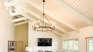 Un vaste salon doté d’un haut plafond, d’un lustre, d’un grand téléviseur à écran plat et d’un coin salon confortable avec des canapés et des fauteuils.