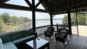Un espace extérieur abrité, doté d’un canapé, de chaises et d’une table, offrant une vue sur un lac avec un quai et de la végétation.