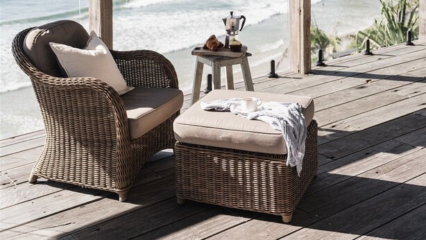 A wicker sofa and ottoman on a wooden deck overlooking the ocean.