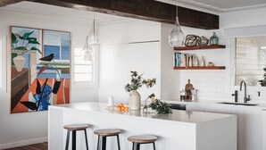 A modern kitchen with a central island, pendant lights, and a large painting on the wall.