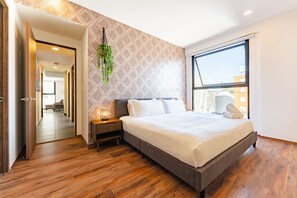 Une chambre moderne avec un grand lit, un plancher en bois, un mur à motifs et une plante suspendue.