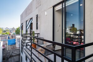 Un bâtiment moderne doté de grandes fenêtres, d’un balcon avec des sièges pour l’extérieur et offrant une vue sur le paysage urbain.