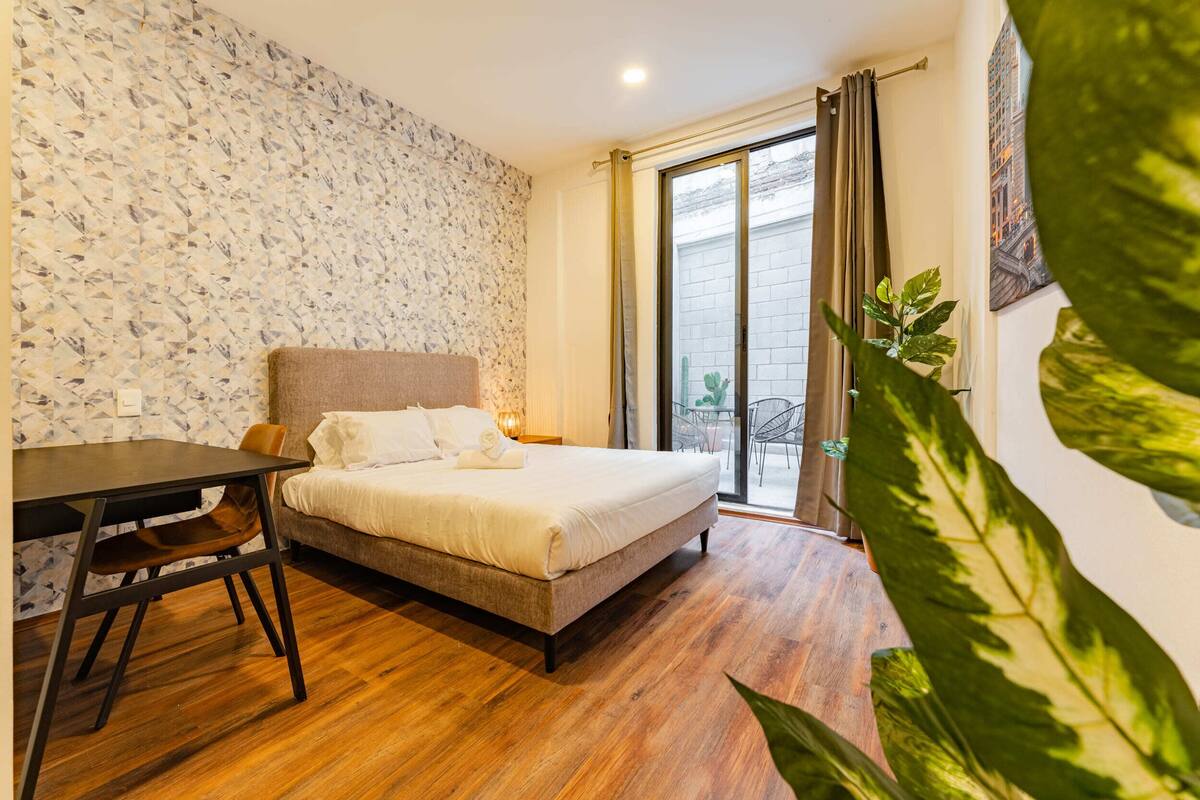 A bedroom with a bed, a desk, and a window with curtains.