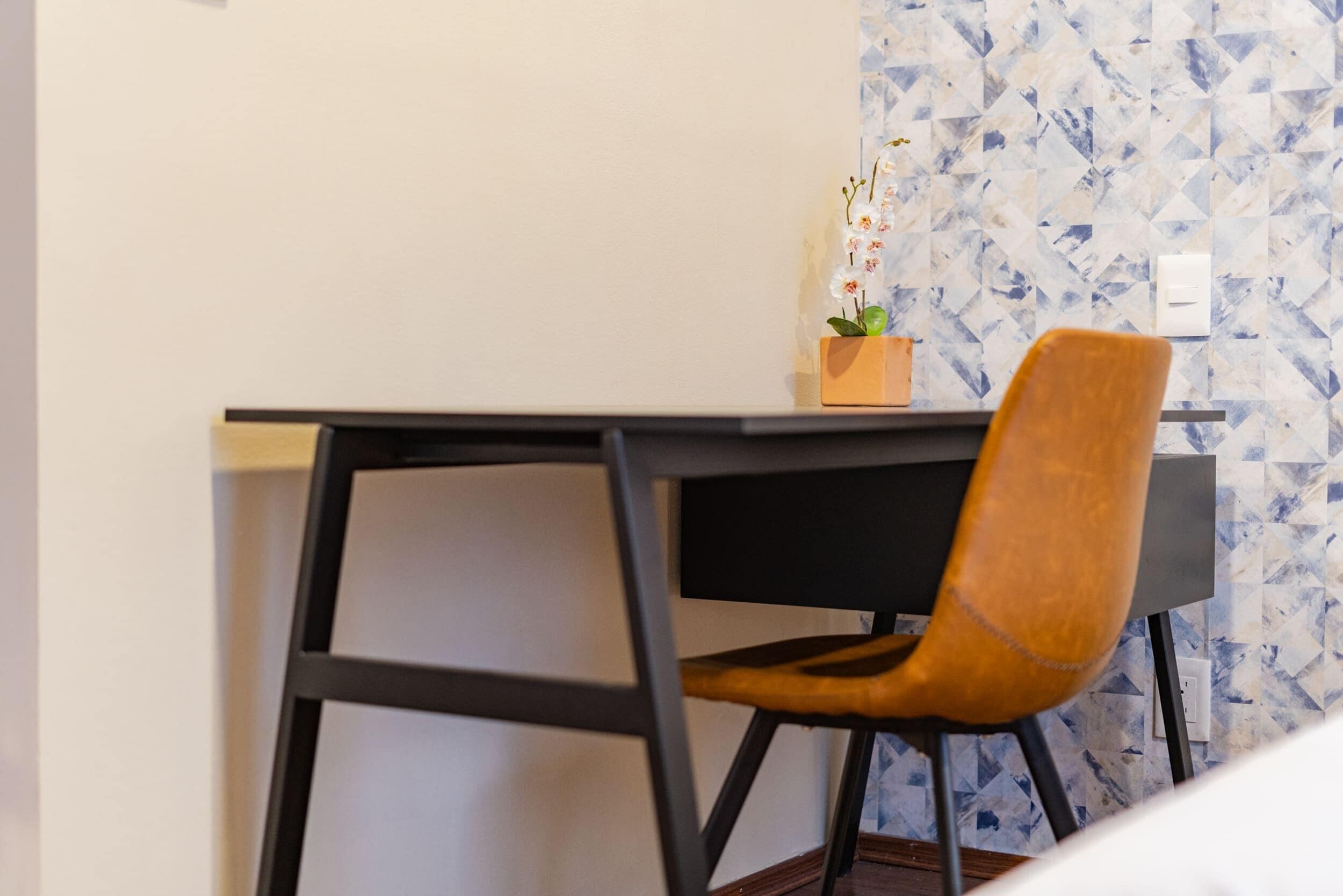 Un bureau avec une chaise, une petite plante et un mur orné d’un motif géométrique.