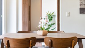 A wooden dining table with two chairs, a potted orchid, and a large window with a view of a plant and a door. - Doctores Apartments by VH (Mexico City)