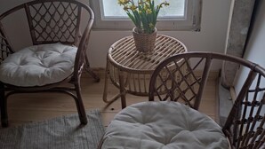 Een kamer met twee rieten stoelen, een klein rond tafeltje met een mand bloemen en een uitzicht op een meer door een groot raam.