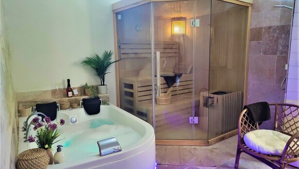 Een moderne badkamer met een vrijstaand bad, een douche met glazen wanden en een rieten stoel.