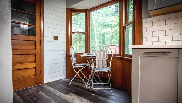 Une cuisine avec une table et des chaises, une porte en bois et une fenêtre donnant sur des arbres.