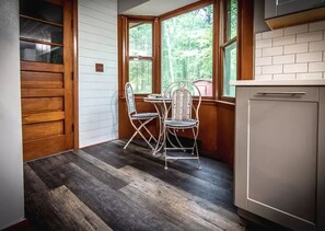 Een keuken met een eettafel en stoelen, een houten deur en een raam met uitzicht op bomen.