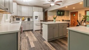 Une cuisine moderne avec des meubles gris, un îlot central et un ventilateur de plafond.