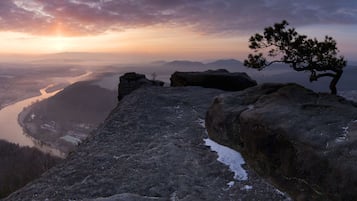 Mirante rochoso com um pinheiro, dando vista para um rio e montanhas ao longe.