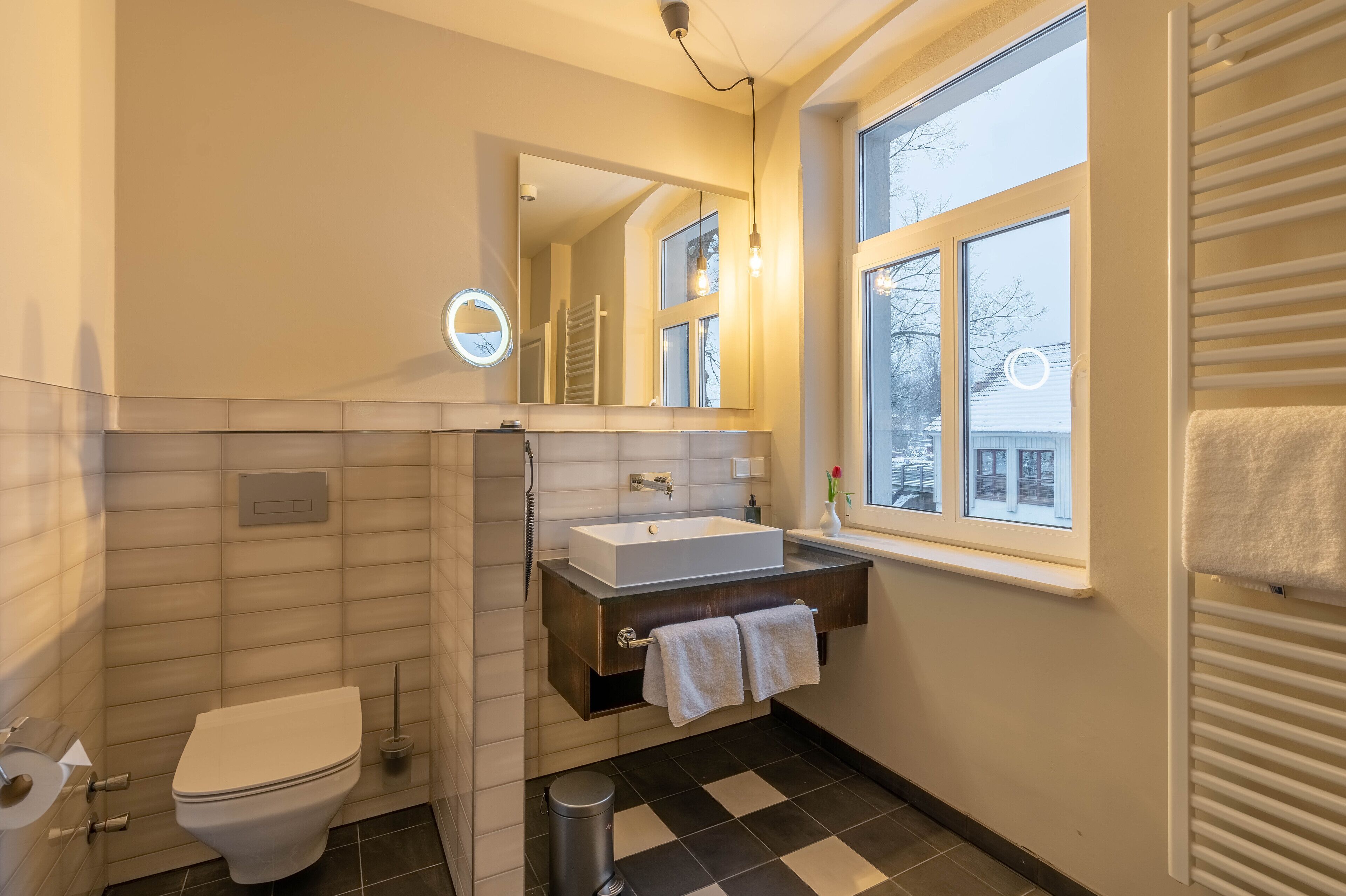 A modern bathroom with a white toilet, a rectangular sink, a mirror, and a window.