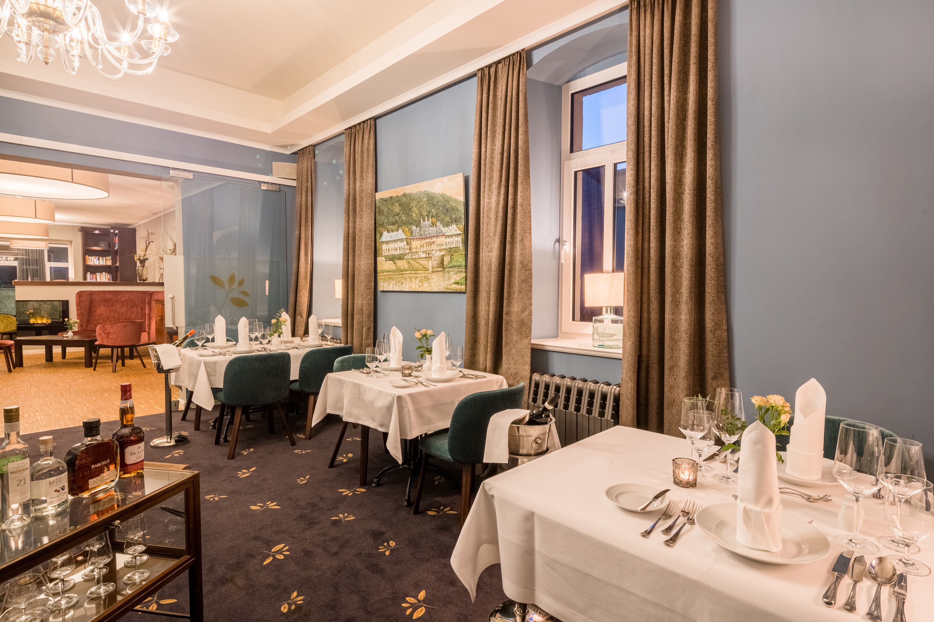 A dining area with tables set for a meal, a chandelier, and a painting on the wall.