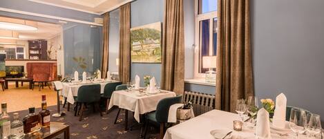 A dining area with tables set for a meal, a chandelier, and a painting on the wall.