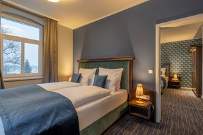 A hotel room with a large bed, a bedside table with a lamp, and a view of the outdoors through a window. - Logis Hotel QUARTIER 5 (Gohrisch)
