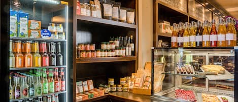 A store with shelves of bottled beverages, jars of preserves, and a display case with pastries.