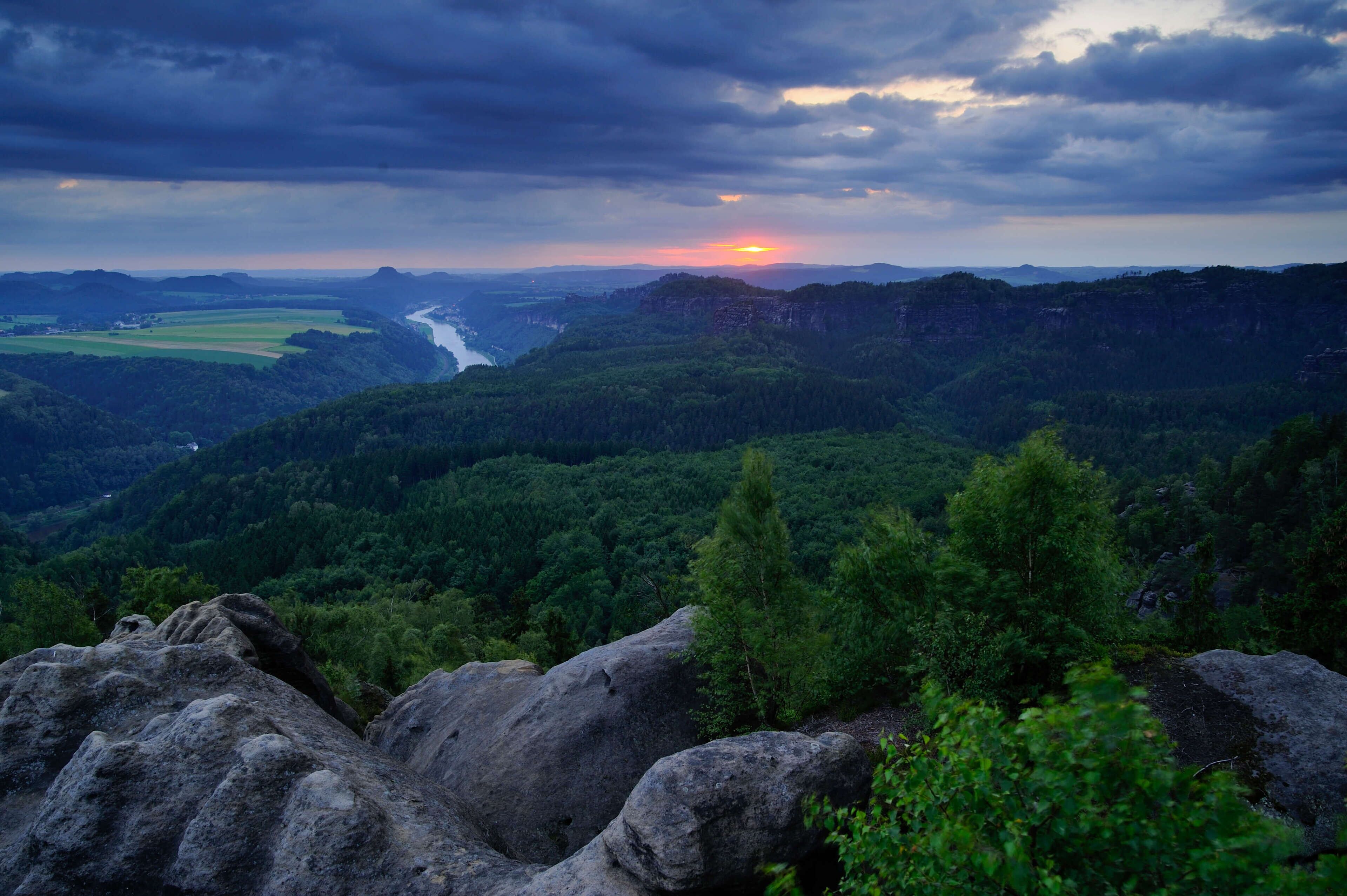 A mountainous landscape with a river, dense forests, and rocky outcrops.