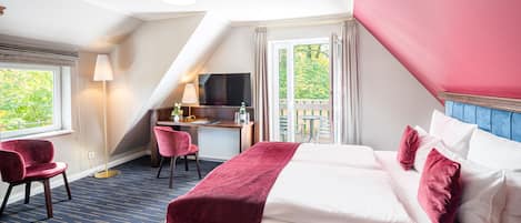 A hotel room with a bed, a desk, a chair, and a view of greenery outside.